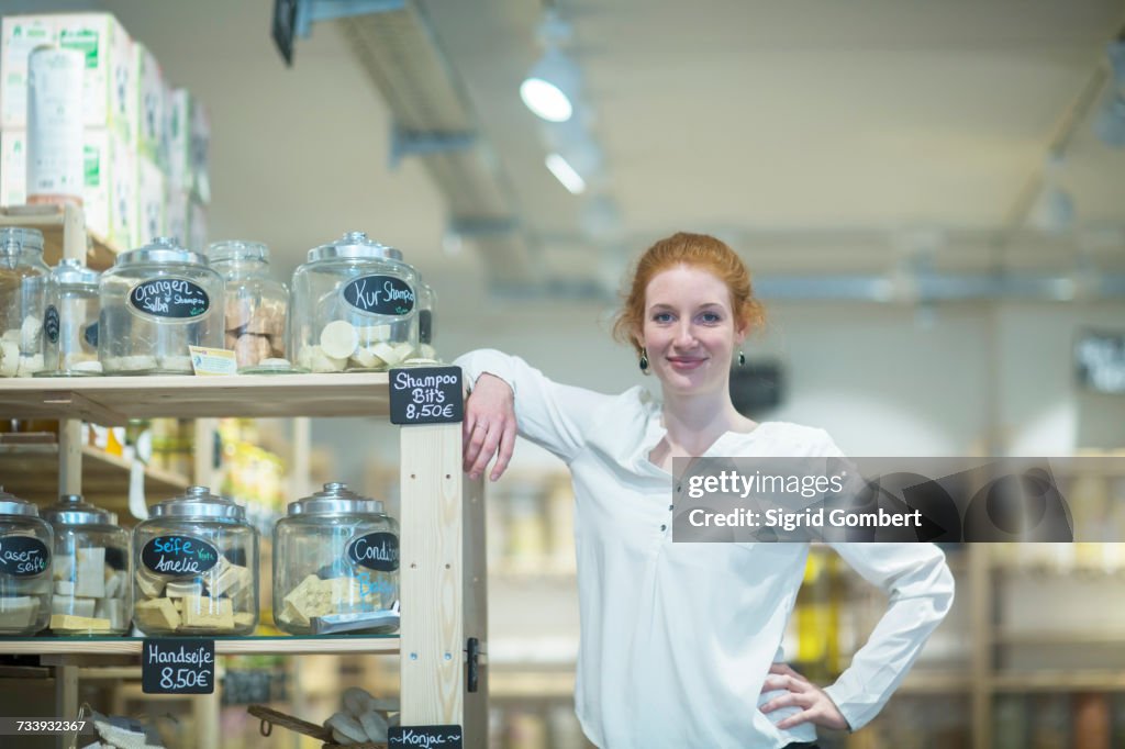 Small business owner leaning against shelves looking at camera