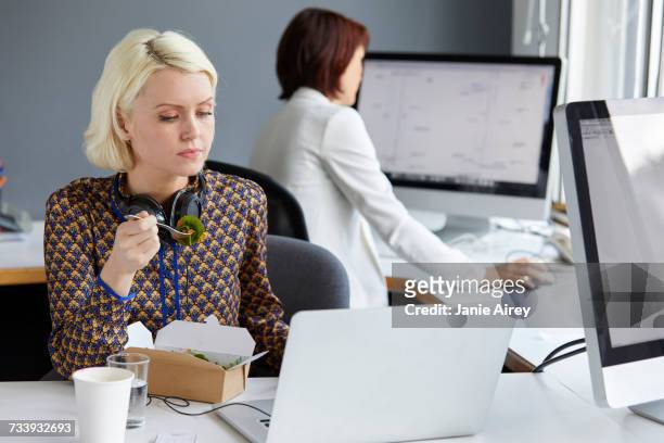 female designer looking at laptop during working lunch at office desk - smart casual lunch stock pictures, royalty-free photos & images