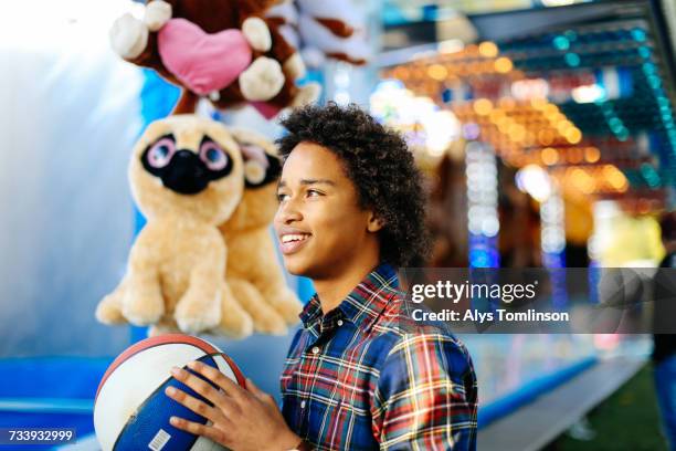 young boy at funfair, playing on fairground stall, holding basketball - fairground stall stock pictures, royalty-free photos & images