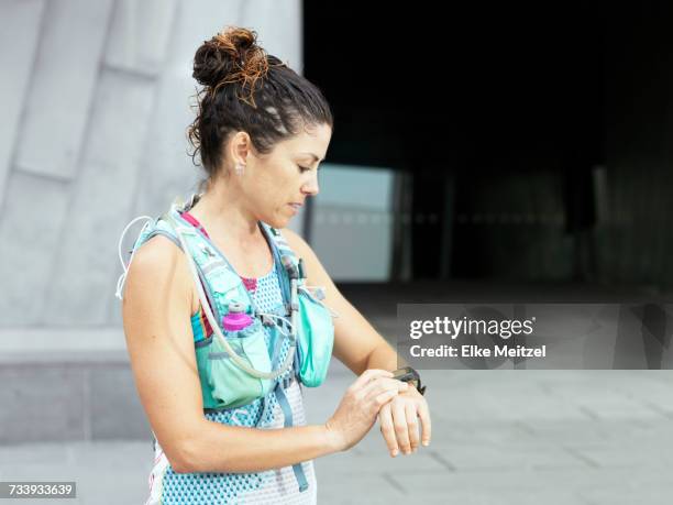 mature female ultra runner looking at smartwatch in city - ultra motivated fotografías e imágenes de stock