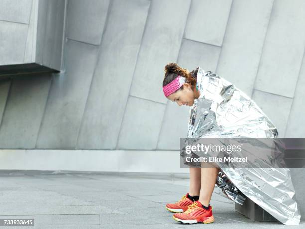 mature female ultra runner wrapped in foil blanket in city - ultra motivated fotografías e imágenes de stock