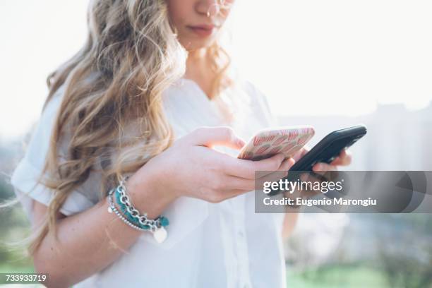 young woman outdoors, looking at two smartphones, mid section - holding two things foto e immagini stock