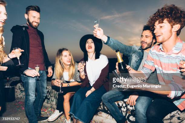 group of friends enjoying roof party, holding champagne glasses, making a toast - champagne rooftop stock pictures, royalty-free photos & images