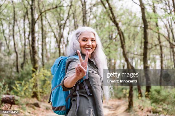 portrait of mature female backpacker giving peace sign in forest, scandicci, tuscany, italy - victory sign stock-fotos und bilder