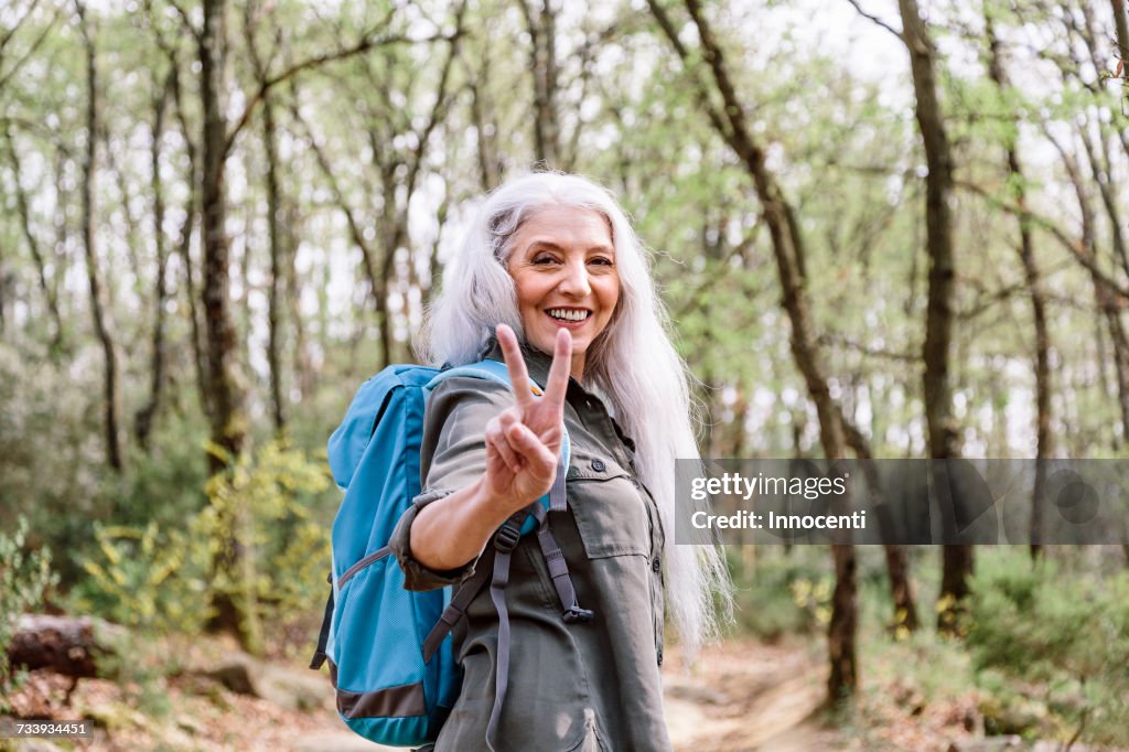 Portrait of mature female backpacker giving peace sign in forest, Scandicci, Tuscany, Italy