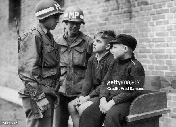 American military police officers with 14 year-old Willy Etschenberg and 10 year-old Hubert Heinrichs, who are being held after sniping at U.S....