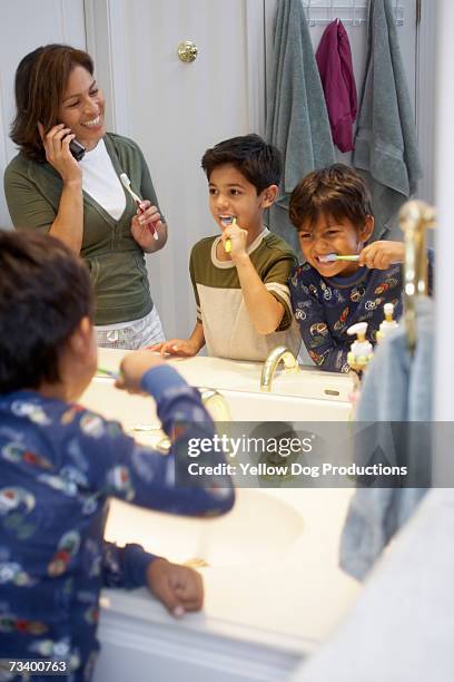 mother and sons (6-8) brushing teeth, woman using cell phone - brush teeth phone stock pictures, royalty-free photos & images