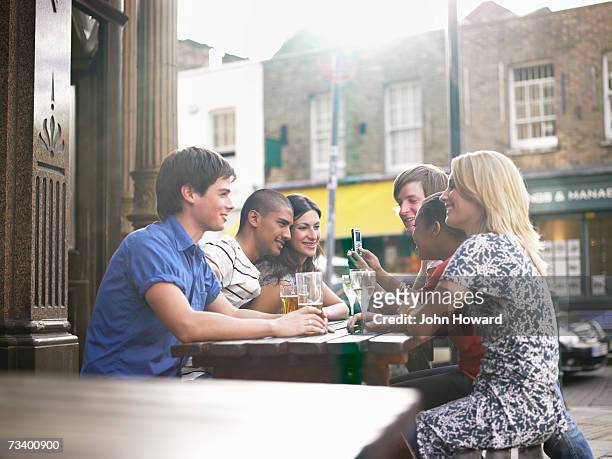six young adults sitting at outdoor pub table, man with mobile phone - london pub stock pictures, royalty-free photos & images