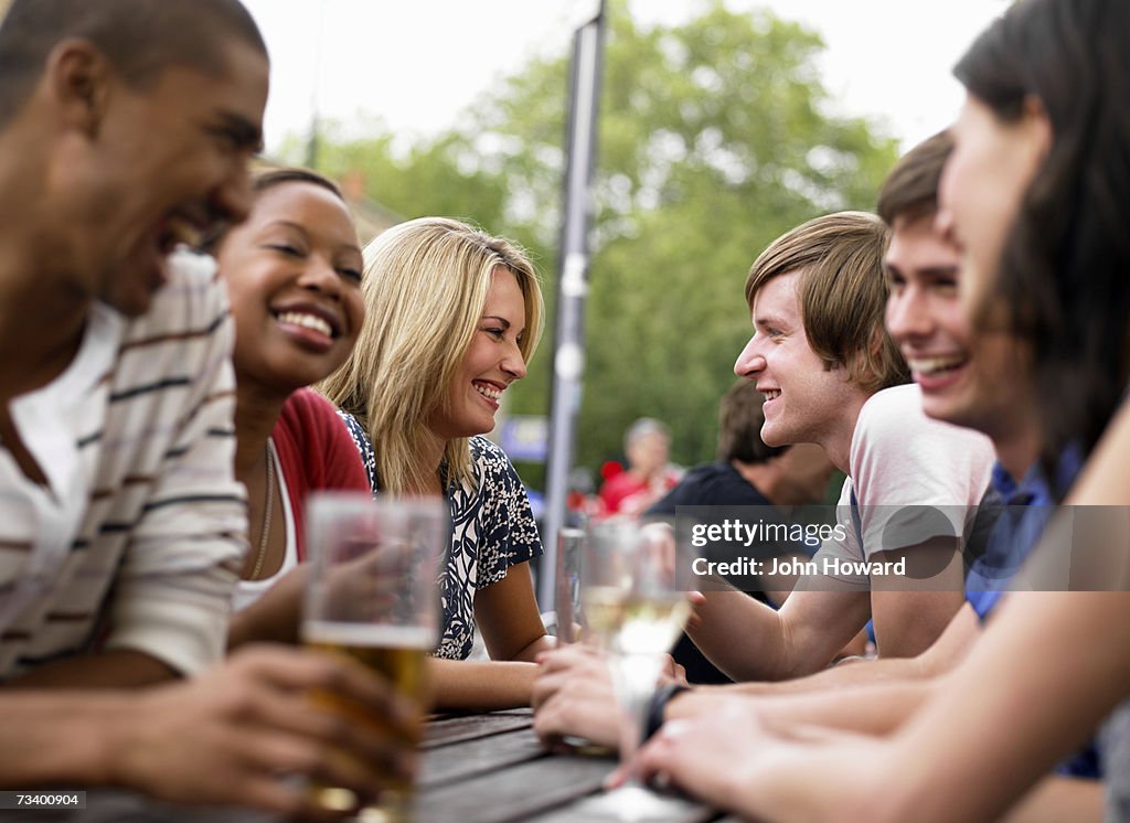 Six young adults sitting at outdoor pub table (differential focus)