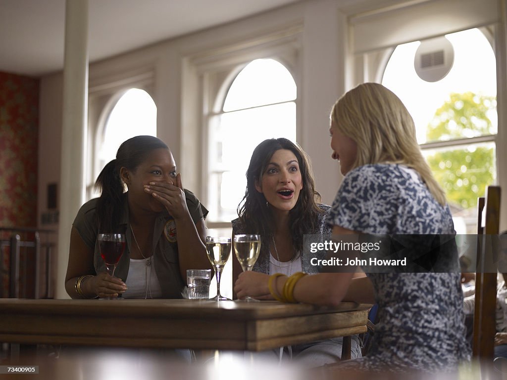 Young woman talking in pub, two friends gasping in response