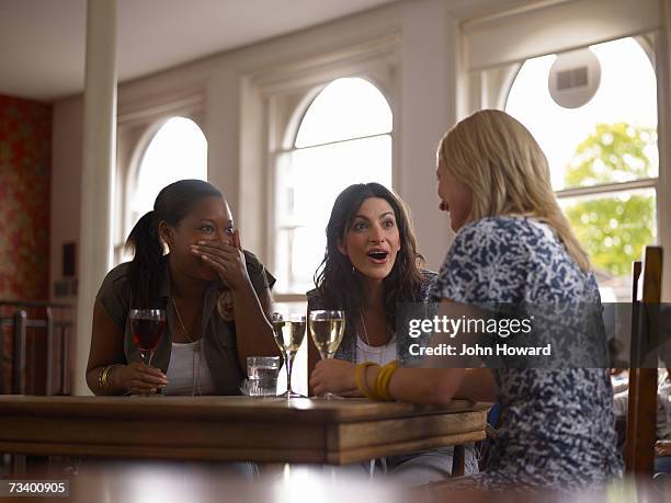 young woman talking in pub, two friends gasping in response - scandal stockfoto's en -beelden