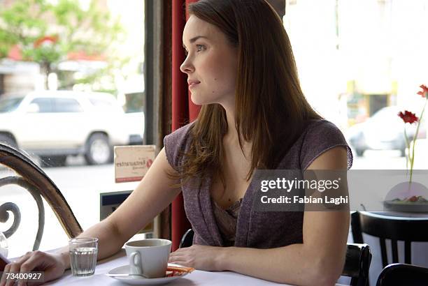 young woman sitting in caft, looking out window - caft stock pictures, royalty-free photos & images