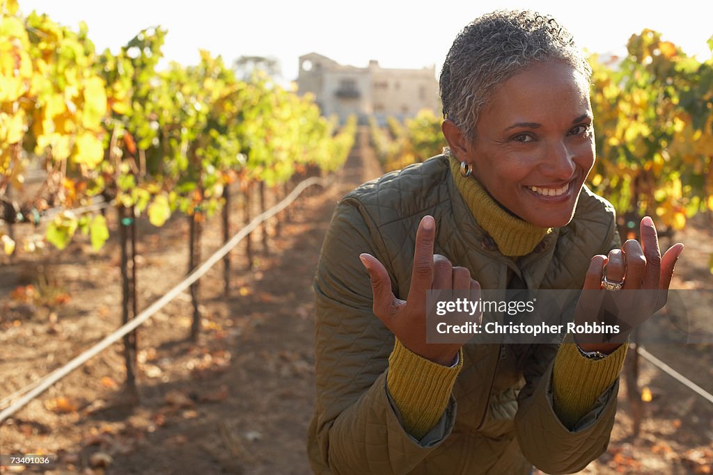 Mature woman standing in vineyard, making hand gestures, smiling