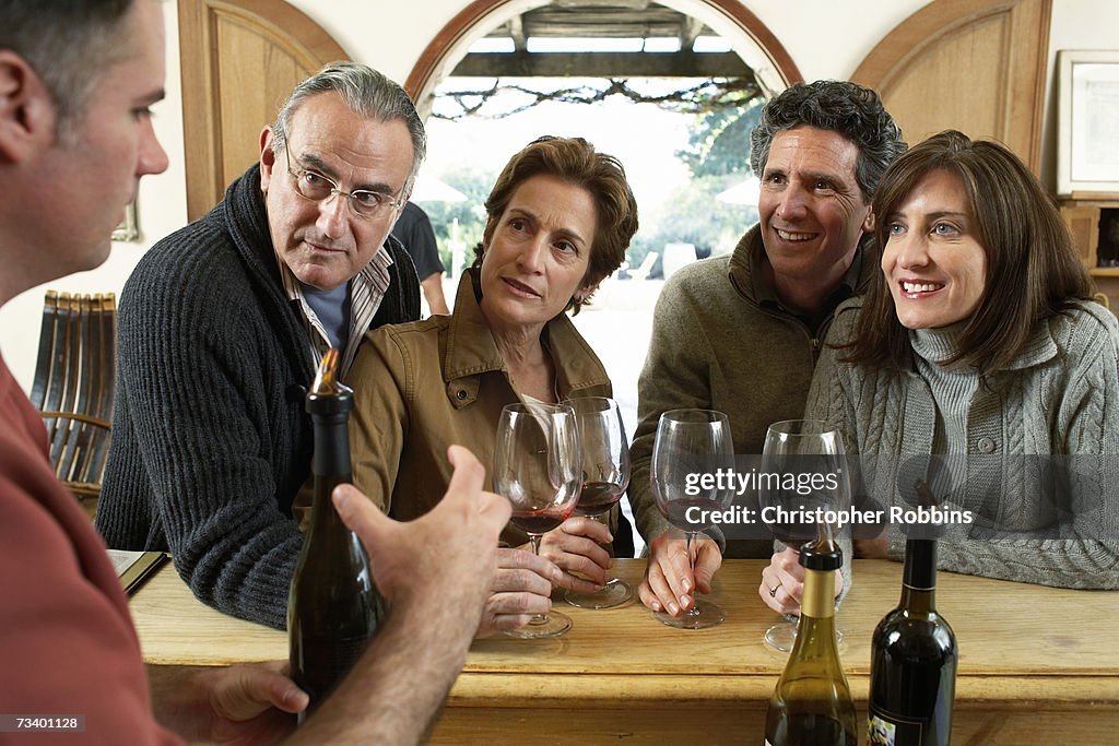 Man discussing wine with mature group at bar counter