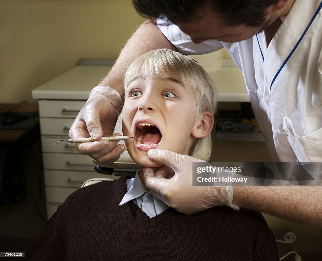 Dentist examining boy's (12-14) teeth, patient looking worried