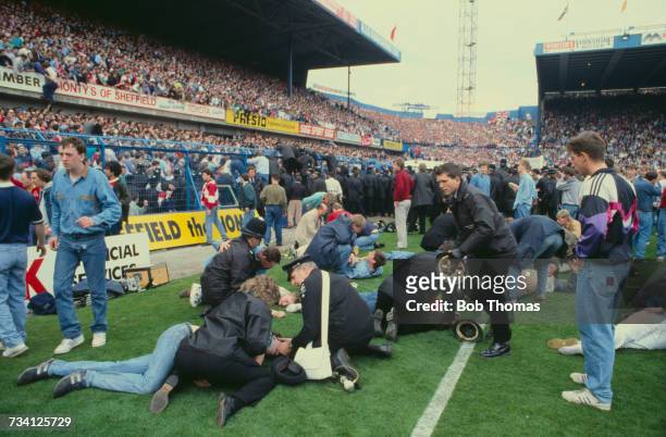 Police officers and a St John Ambulance volunteer attend to casualties on the pitch at Hillsborough football stadium in Sheffield, after a human...