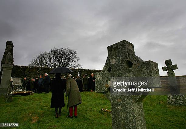 Family members and friends stand at the graveside of Chief of Clan MacLeod, John MacLeod at the burial ground of the old ruined church at Kilmuir,...