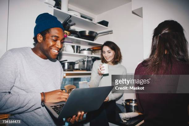 happy man showing laptop to female friend with coffee cup in kitchen - happy friends stockfoto's en -beelden