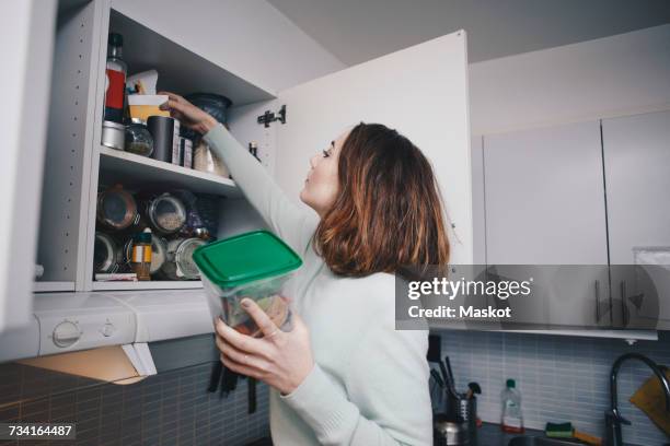 young woman searching in cabinet at kitchen - kitchen pantry ストックフォトと画像