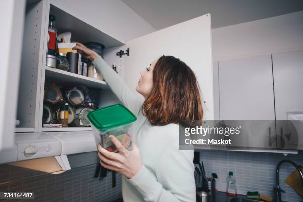 young woman searching in cabinet at kitchen - kitchen cabinets stock pictures, royalty-free photos & images