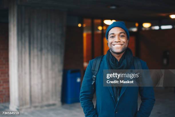 portrait of happy man wearing blue warm clothing and knit hat standing in campus - university student portrait stock pictures, royalty-free photos & images