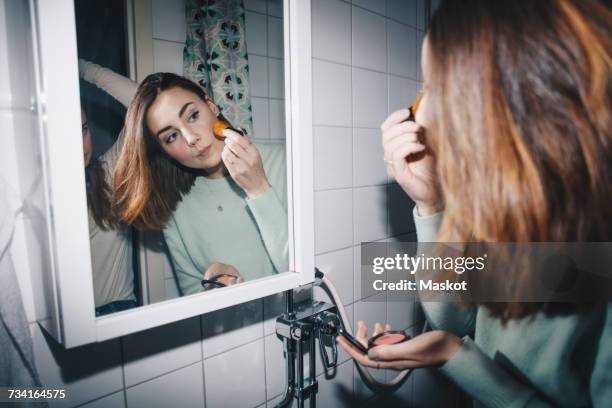 young woman applying blush looking in mirror at college dorm bathroom - schminkpinsel stock-fotos und bilder