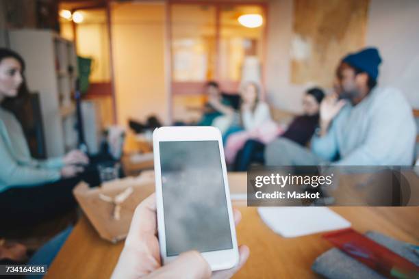 cropped hand woman using mobile phone against friends in college dorm room - studenten bildschirm stock-fotos und bilder