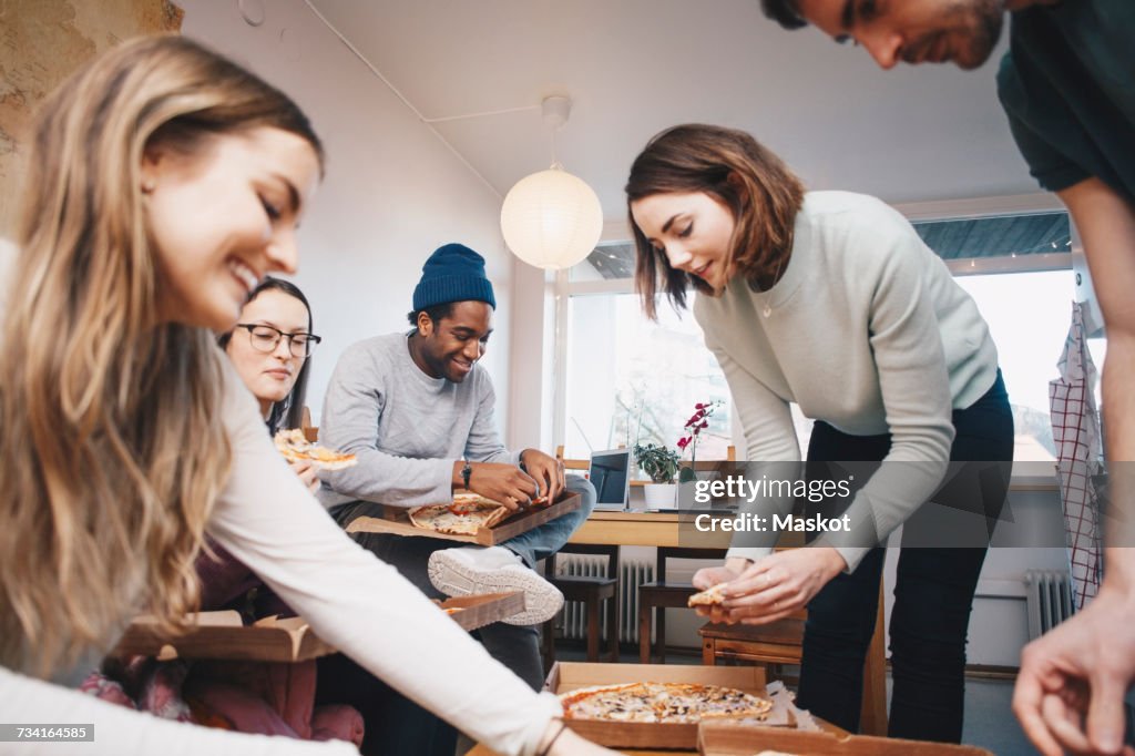 Happy young friends eating pizza in college dorm room