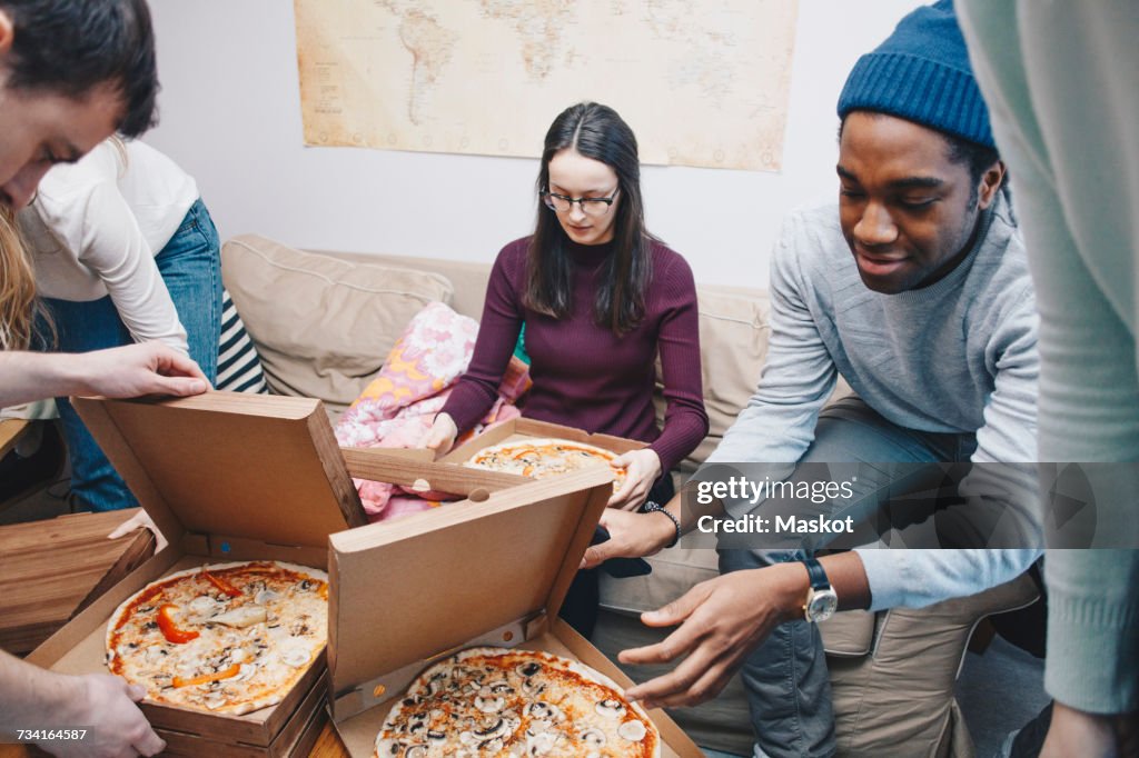 High angle view of young friends opening pizza boxes in dorm room
