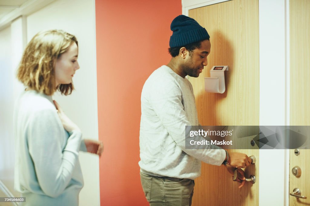 Woman looking at male friend opening door lock in college dorm