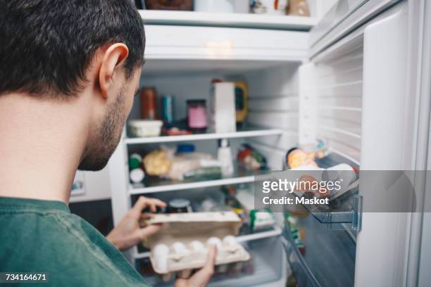man holding egg carton by refrigerator in kitchen - frigorífico fotografías e imágenes de stock