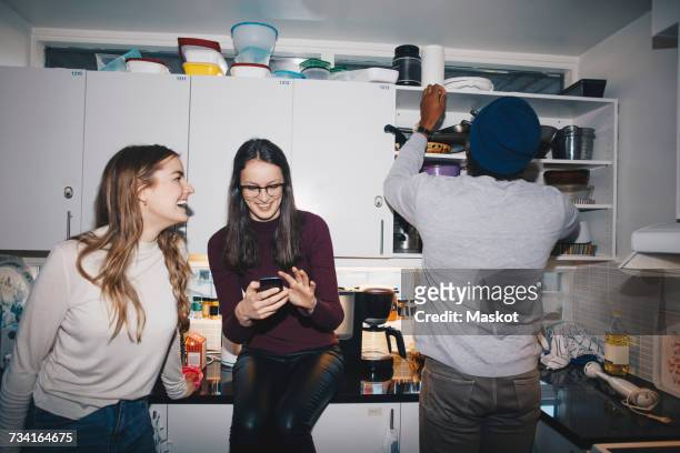 female friends enjoying by man in kitchen at college dorm - male student wearing glasses with friends stockfoto's en -beelden