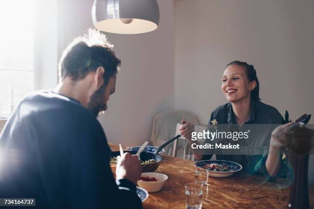 happy woman with mobile phone looking at man while eating pasta at home - 30s woman eating stock pictures, royalty-free photos & images