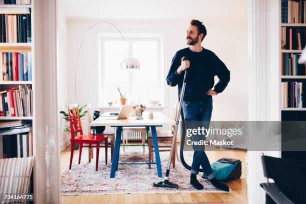 happy man standing with vacuum cleaner in dining room at home - poetsen stockfoto's en -beelden