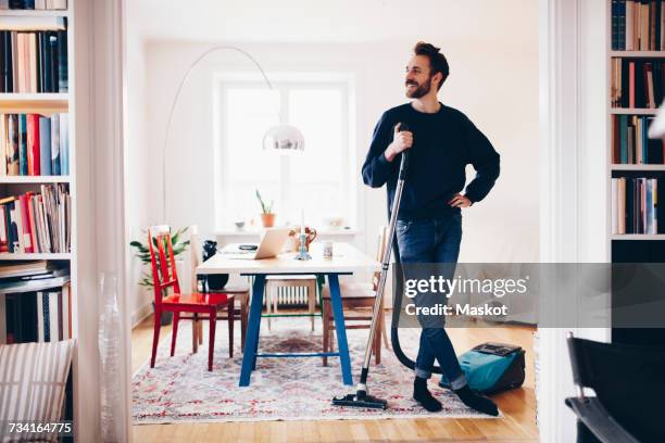 happy man standing with vacuum cleaner in dining room at home - cleaning equipment stock pictures, royalty-free photos & images