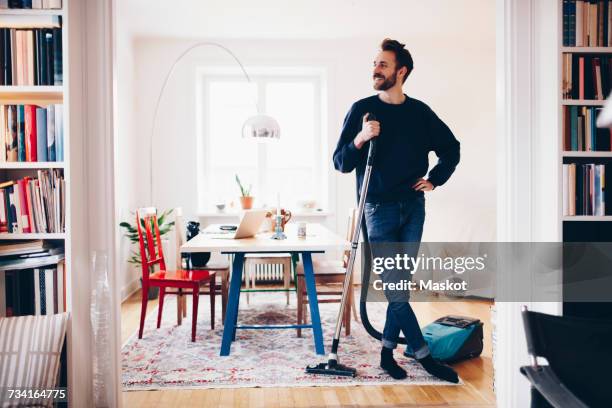 happy man standing with vacuum cleaner in dining room at home - dammsugare bildbanksfoton och bilder