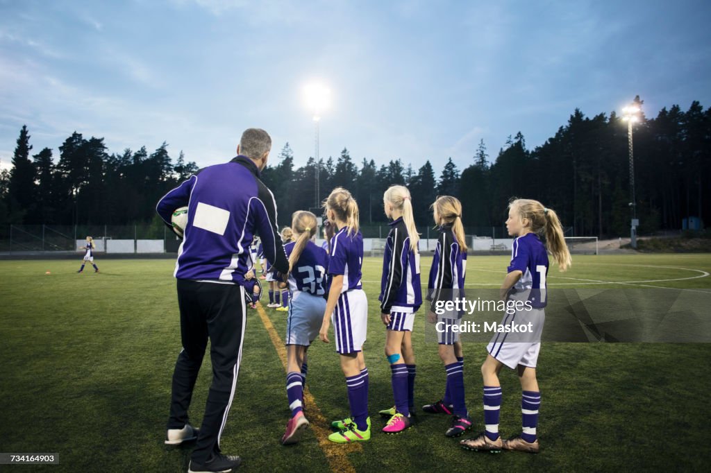 Coach explaining female soccer team on field against sky