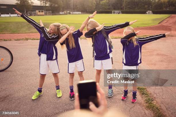 cropped girl photographing friends performing dab dance on footpath against soccer field - dab dance stock pictures, royalty-free photos & images