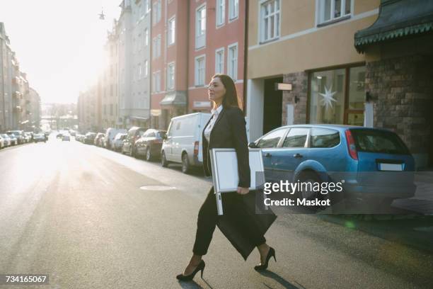 side view of female real estate agent carrying signboard and bag while crossing street in city - tacchi a spillo foto e immagini stock