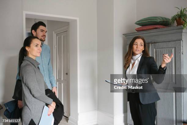 female real estate agent pointing while standing with young couple at home - selling house stockfoto's en -beelden