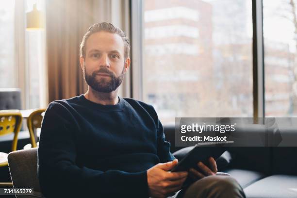 portrait of confident businessman holding digital tablet at brightly lit office lobby - corporate portraits man stockfoto's en -beelden