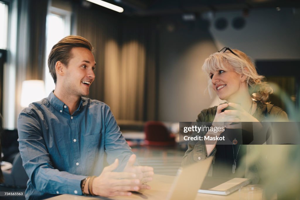 Happy business colleagues discussing at conference table in board room