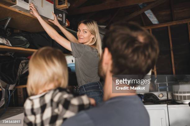 mid adult woman arranging box on shelf while looking at family in storage room - woman reaching stock pictures, royalty-free photos & images