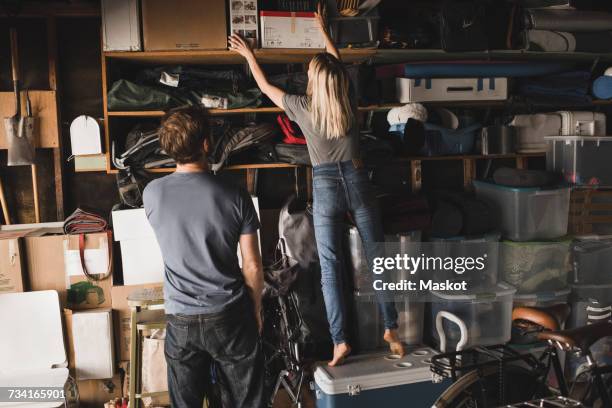 rear view of man looking at woman arranging boxes on shelf in storage room - storage compartment stock pictures, royalty-free photos & images