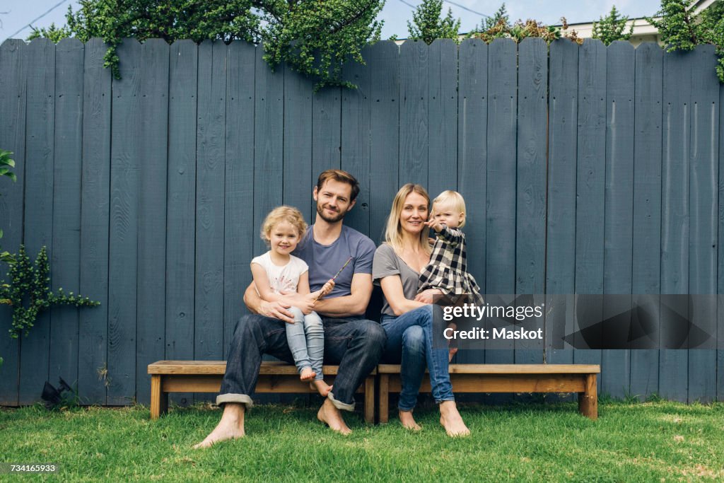 Full length portrait of happy parents and children sitting on seats against fence at yard