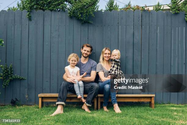 full length portrait of happy parents and children sitting on seats against fence at yard - wooden bench stock pictures, royalty-free photos & images