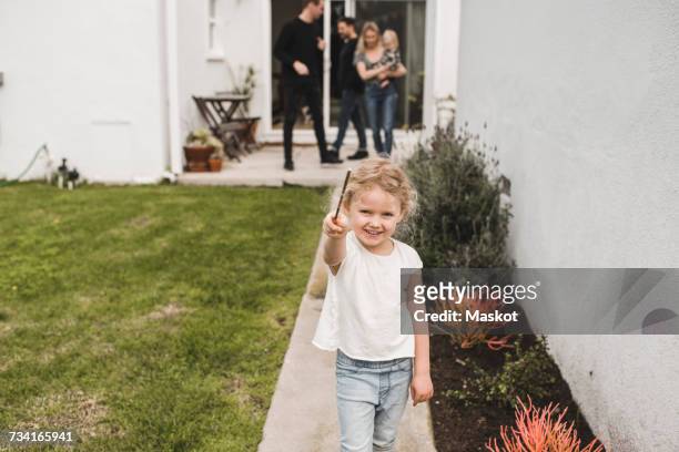 portrait of girl showing magic wand with family in background at yard - magic wand stockfoto's en -beelden