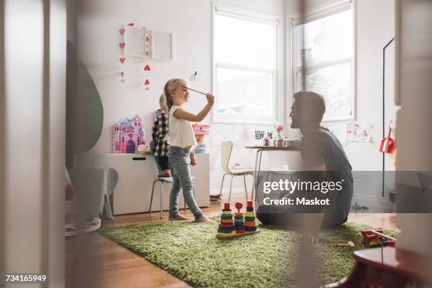 father looking at daughters playing with toy in playroom at home - 不思議グッズ ストックフォトと画像