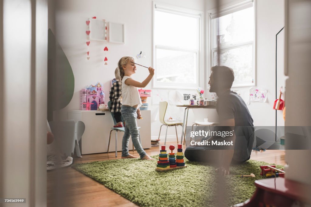 Father looking at daughters playing with toy in playroom at home