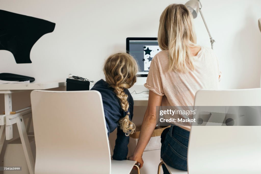 Rear view of girl with mother using laptop at home